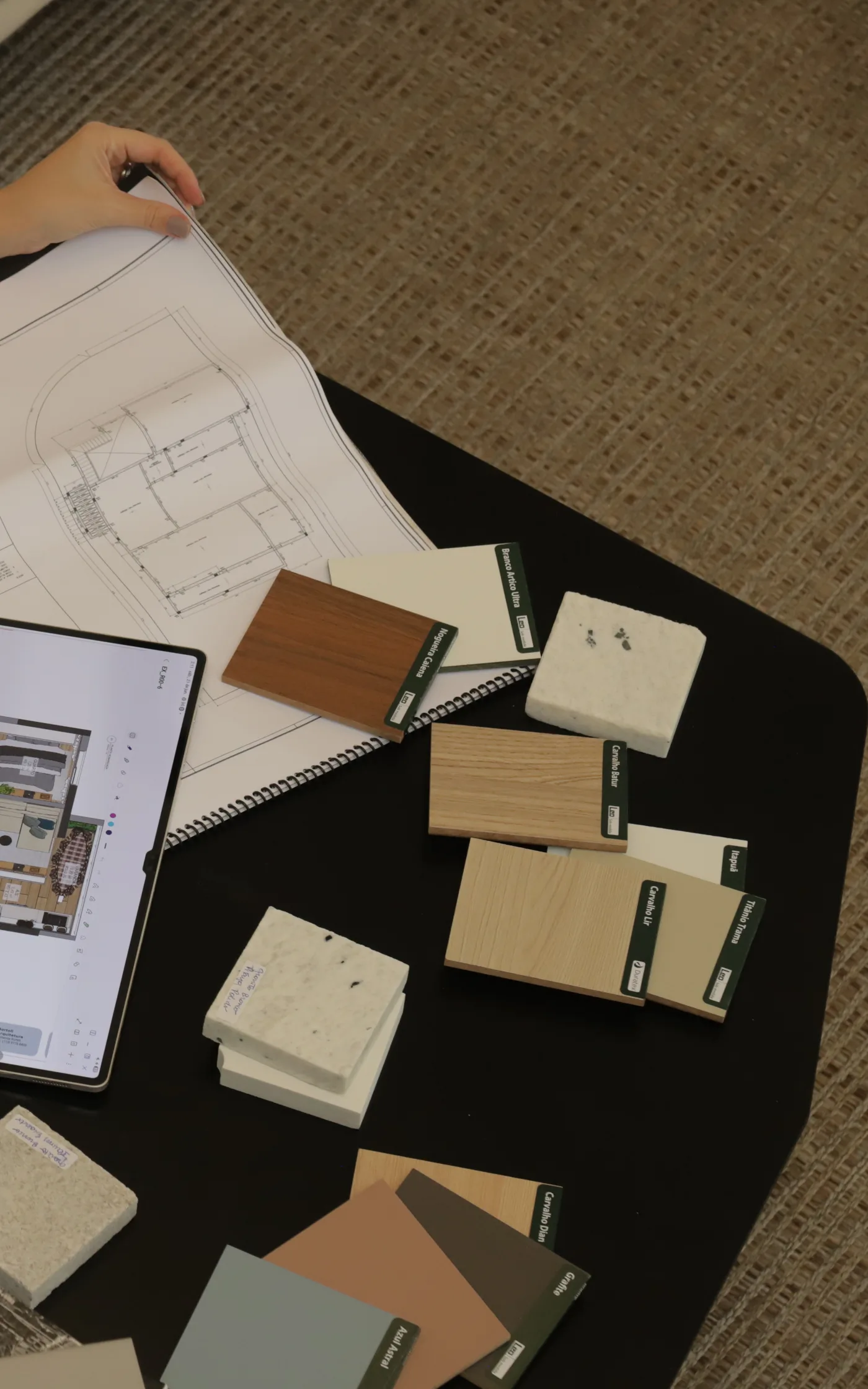 Mesa de trabalho do escritório com planta impressa, projeto no tablet e amostras de madeira, pedra e cores