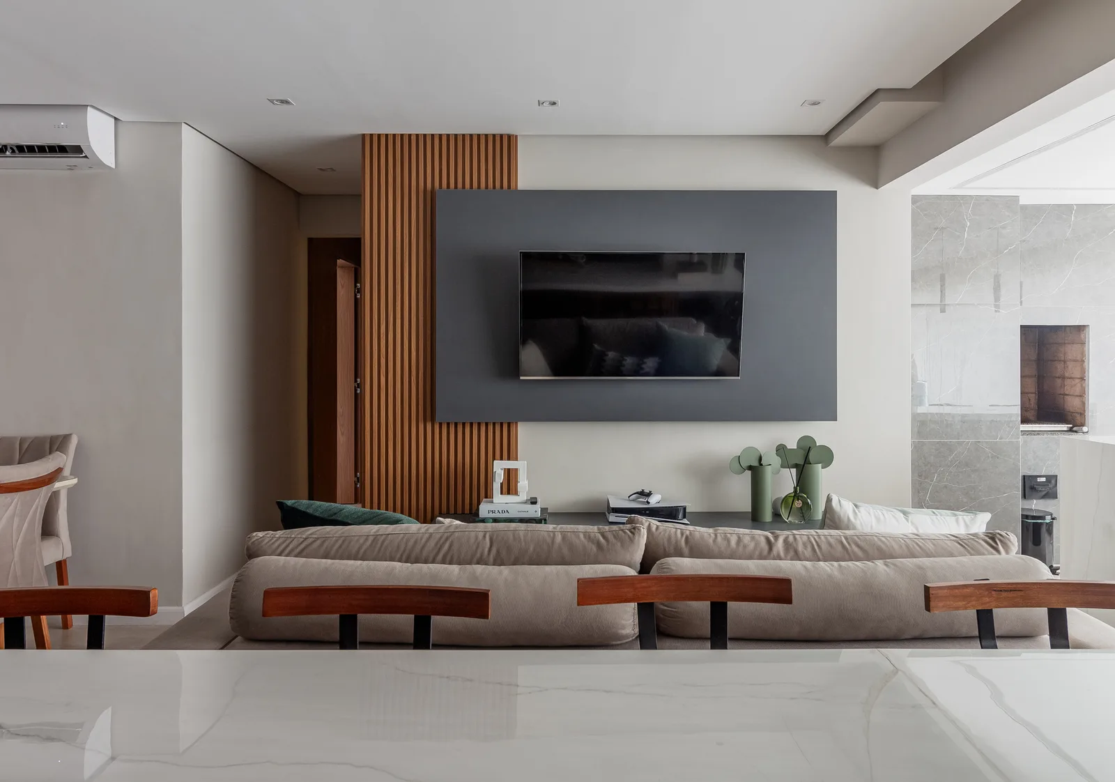 Sala de estar com painel de TV cinza, ripado de madeira e sofá bege