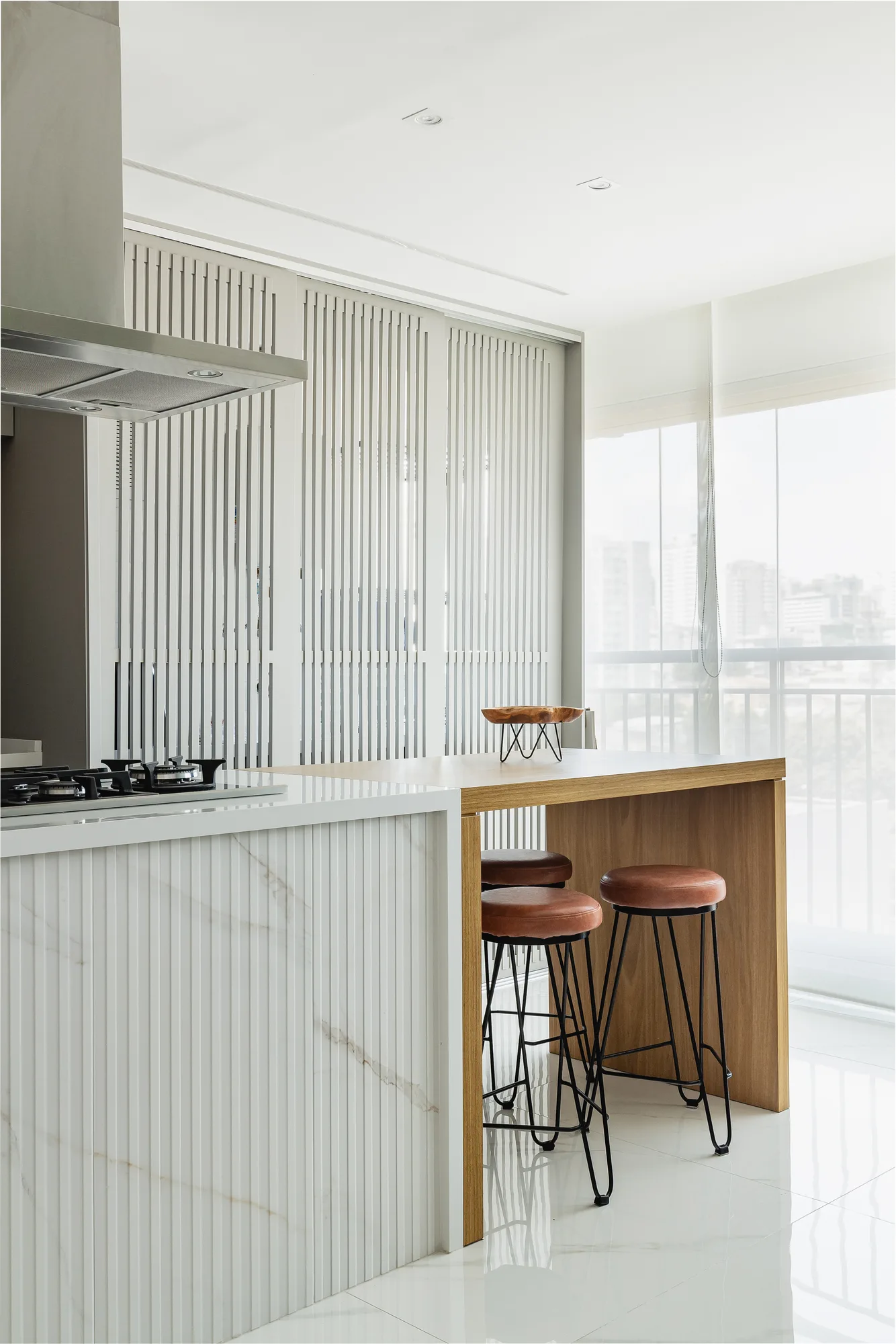 Ilha de cozinha em mármore branco com banquetas e varanda ao fundo