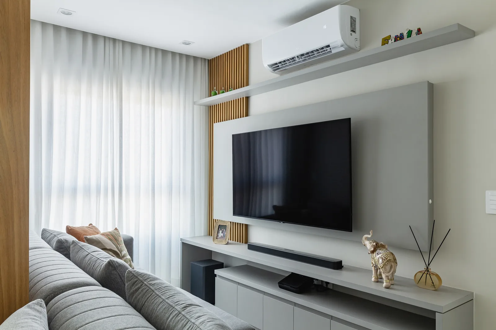 Sala de estar com cortina voil, painel de TV e ripado de madeira