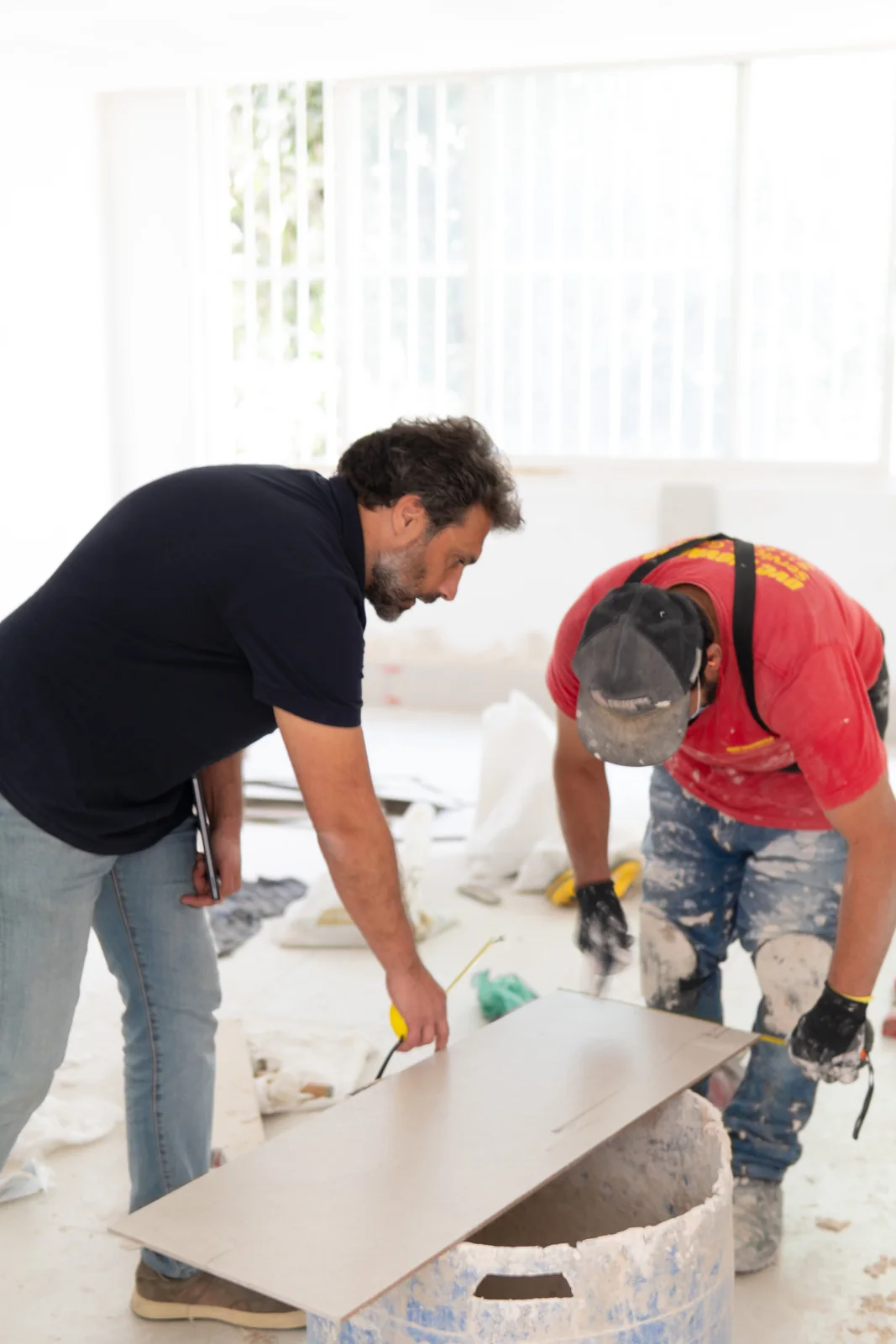 Profissional do escritório e pedreiro medindo uma placa de porcelanato no canteiro de obras