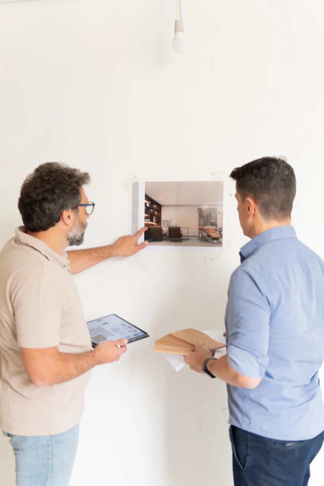 Dois profissionais do escritório analisando o render do projeto colado na parede da obra, com prancheta e amostras de madeira