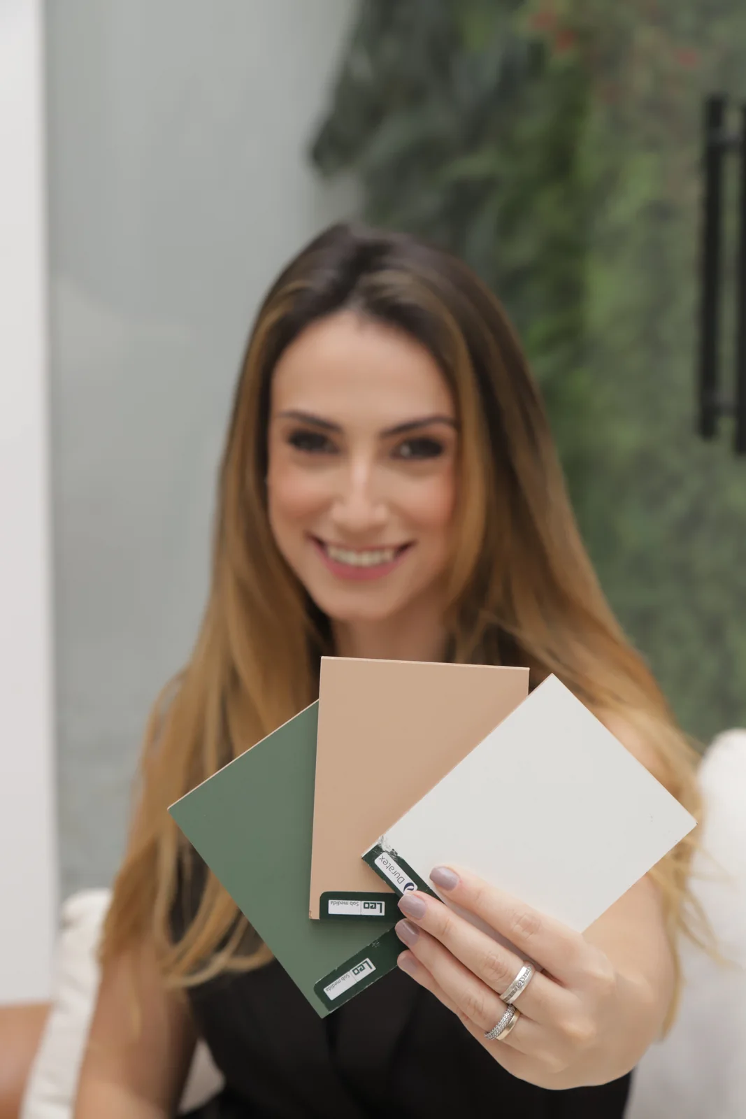 Arquiteta do escritório sorrindo enquanto apresenta amostras de acabamento em verde, terracota e branco